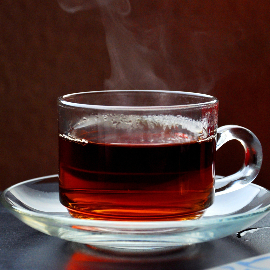 Steaming glass cup of tea on a saucer with a dark background